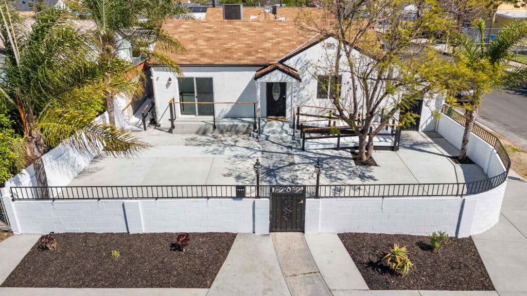A white house with a fence and palm trees in the foreground