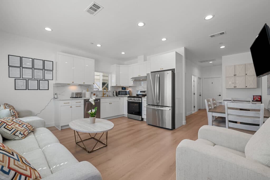 A sleek, modern kitchen flows into a bright living room, featuring minimalist decor and open space for relaxation.