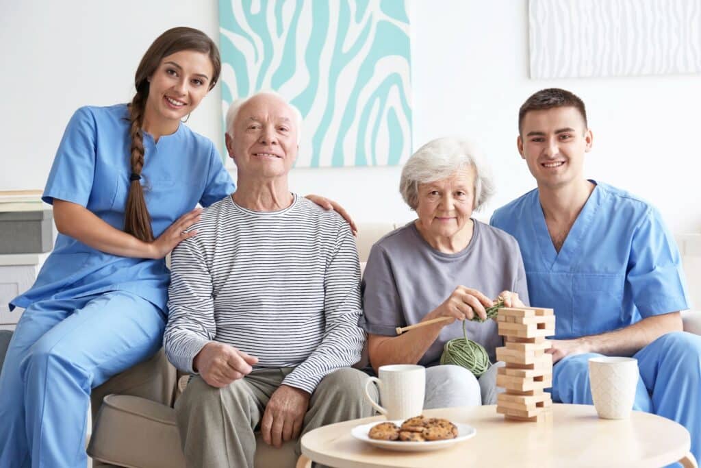 A group of healthcare professionals in scrubs sitting together on a couch, smiling and engaged in conversation.